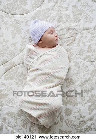 Stock Image - Swaddled Asian baby sleeping on bed. Fotosearch