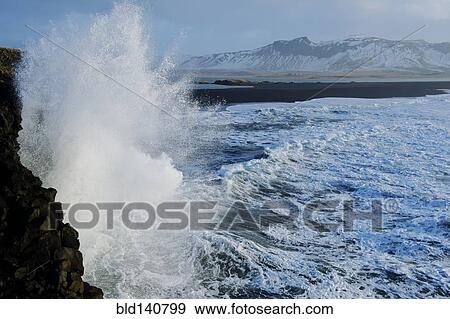 Stock Photo - Waves splashing on rocky cliffs on beach. Fotosearch