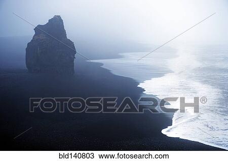 Stock Image - Waves washing up by rock formation on beach. Fotosearch
