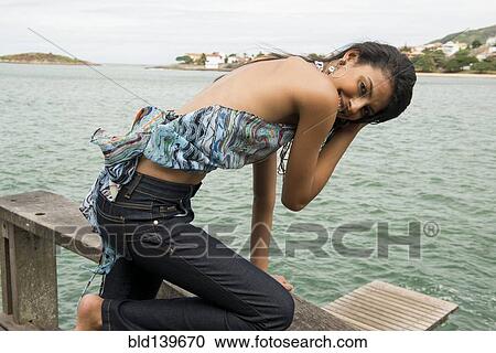 Stock Image - Woman kneeling on banister overlooking harbor. Fotosearch