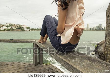 Stock Photo - Woman sitting on banister overlooking urban harbor. Fotosearch