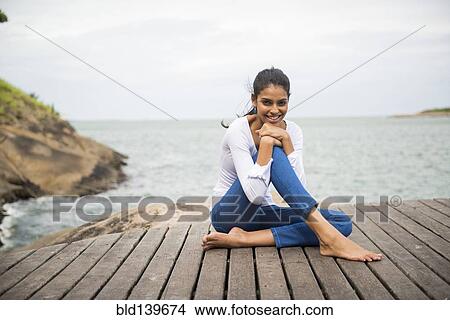 Picture - Woman sitting on wooden deck overlooking lake. Fotosearch