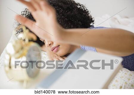 Stock Photo - Woman turning off alarm clock in bedroom. Fotosearch