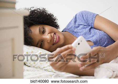 Stock Image - Woman using cell phone in bed. Fotosearch