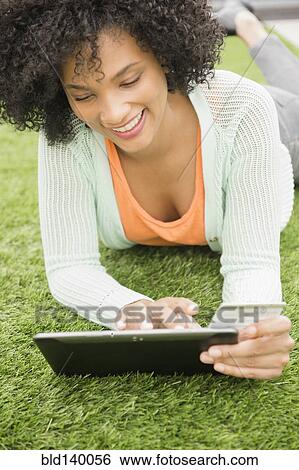 Stock Photograph - Woman using digital tablet on grassy lawn. Fotosearch