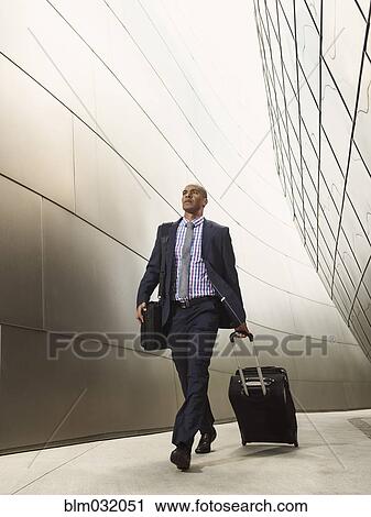 Stock Image - Black businessman rolling luggage. Fotosearch