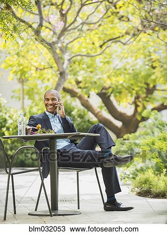 Stock Image - Black businessman working and eating lunch outdoors. Fotosearch