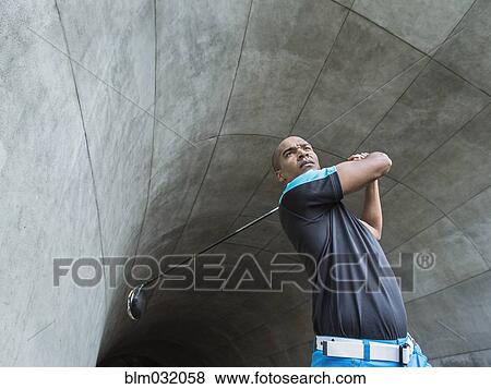 Stock Photo - Black man playing golf in urban tunnel. Fotosearch