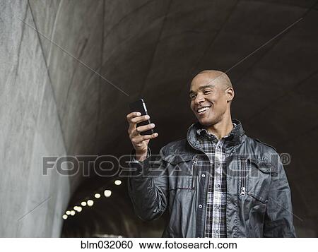 Stock Image - Black man using cell phone in urban tunnel. Fotosearch