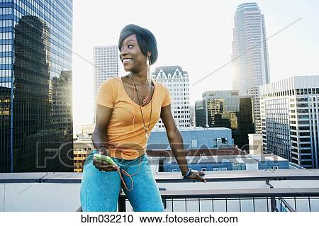 Black woman listening to earbuds on urban rooftop View Large Photo Image Stock Image - Black woman listening to earbuds on urban rooftop. Fotosearch
