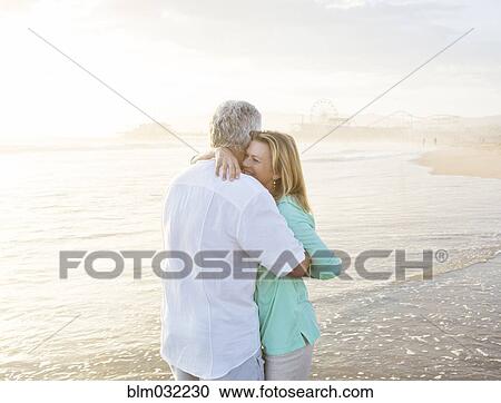 Stock Image - Caucasian couple hugging on beach. Fotosearch