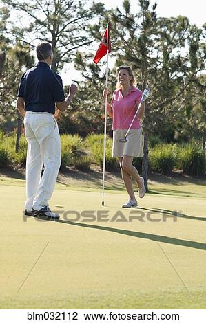 Stock Image - Caucasian couple playing golf on course. Fotosearch