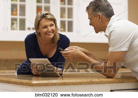 Caucasian couple using digital tablet and cell phone at kitchen counter View Large Photo Image Stock Image - Caucasian couple using digital tablet and cell phone at kitchen counter. Fotosearch