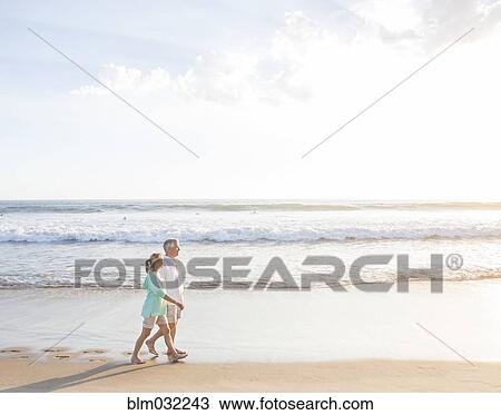 Stock Image - Caucasian couple walking on beach. Fotosearch