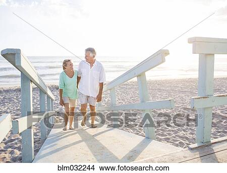Picture - Caucasian couple walking on wooden boardwalk on beach. Fotosearch