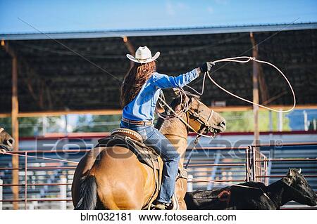 Stock Image - Caucasian cowgirl on horse throwing lasso in rodeo on ranch. Fotosearch