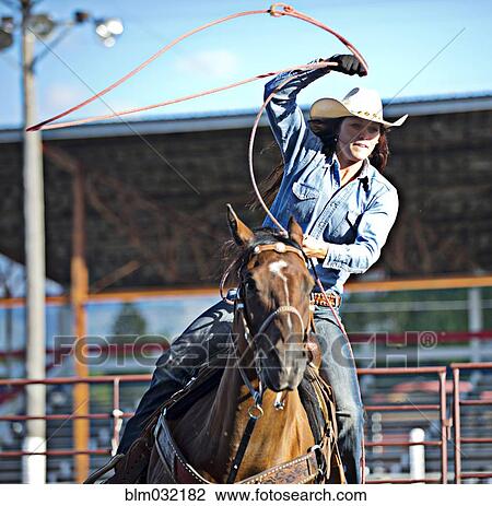 Stock Image - Caucasian cowgirl on horse throwing lasso in rodeo on ranch. Fotosearch