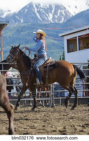 Stock Photograph - Caucasian cowgirl riding horse in rodeo on ranch. Fotosearch