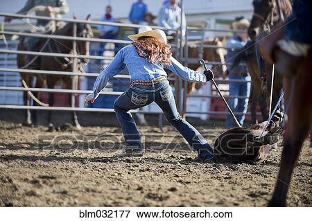 Stock Photo - Caucasian cowgirl tying horse in rodeo on ranch. Fotosearch