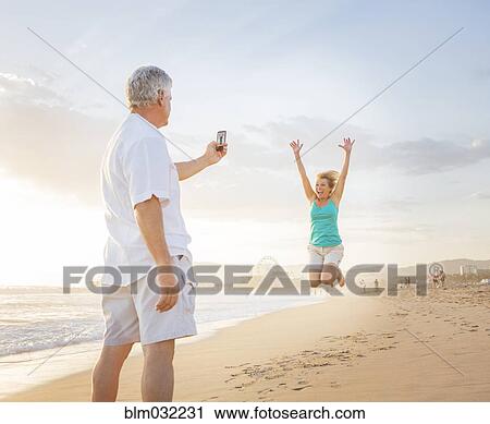 Caucasian man taking cell phone photograph of wife on beach View Large Photo Image Stock Image - Caucasian man taking cell phone photograph of wife on beach. Fotosearch