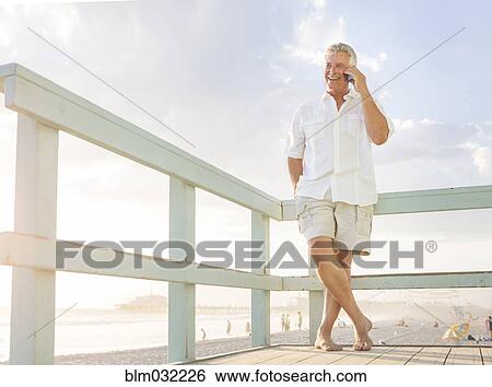 Stock Photograph - Caucasian man talking on cell phone on boardwalk at beach. Fotosearch