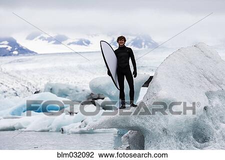 Stock Image - Caucasian surfer carrying board near glacial water. Fotosearch