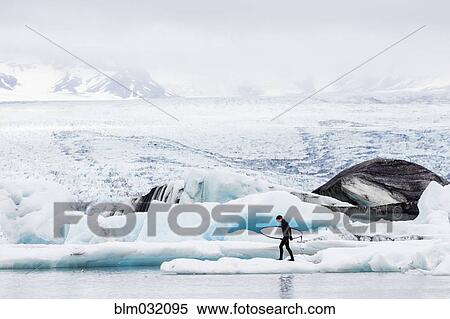 Stock Photography - Caucasian surfer carrying board near glacial water. Fotosearch