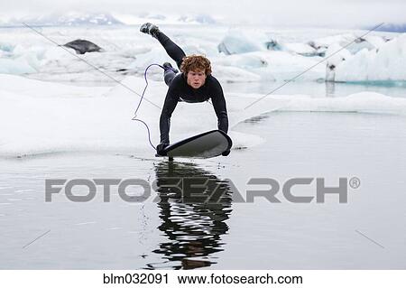 Stock Image - Caucasian surfer leaping on board in glacial water. Fotosearch
