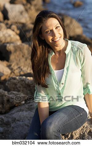 Picture - Caucasian woman smiling on rocky beach. Fotosearch