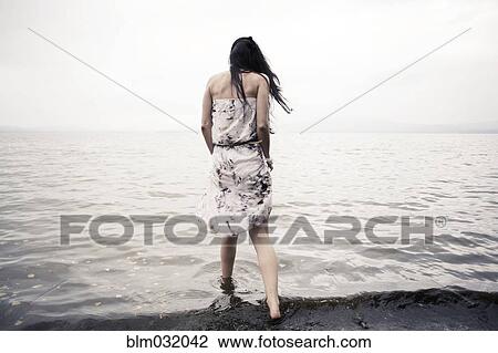 Stock Image - Caucasian woman wading in water on beach. Fotosearch