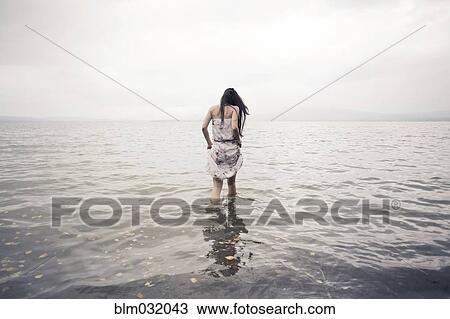 Stock Image - Caucasian woman wading in water on beach. Fotosearch