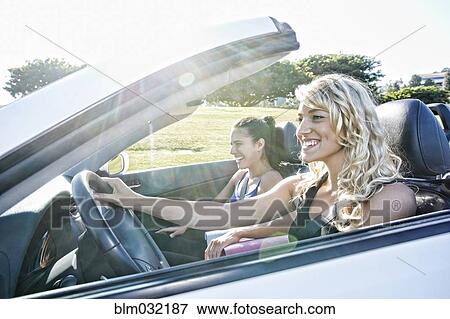 Stock Photo - Excited women driving convertible on road trip. Fotosearch