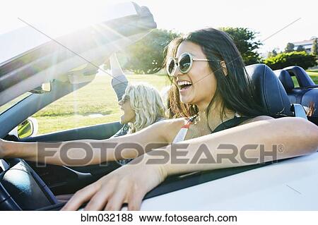 Stock Photo - Excited women driving convertible on road trip. Fotosearch