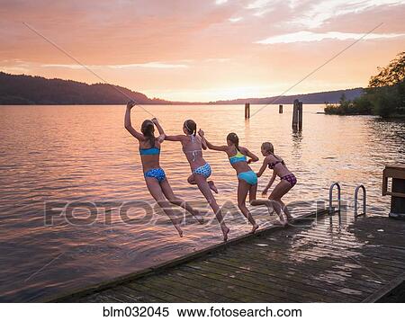 Stock Photography - Girls jumping into lake from wooden dock. Fotosearch