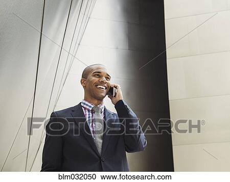 Stock Image - Low angle view of Black businessman talking on cell phone. Fotosearch