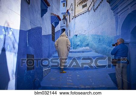 Picture - Man photographing hooded man on colorful historical village steps, Chefchaouen, Chefchaouen, Morocco. Fotosearch