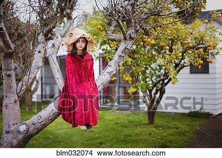 Picture - Mixed race girl in witch costume sitting in tree. Fotosearch