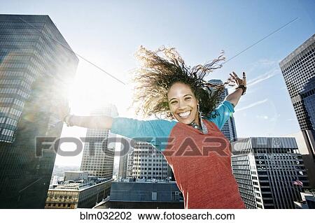 Mixed race woman cheering with arms outstretched on urban rooftop View Large Photo Image Stock Image - Mixed race woman cheering with arms outstretched on urban rooftop. Fotosearch