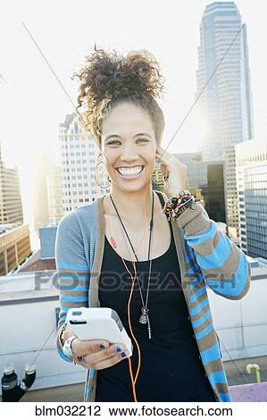Stock Image - Mixed race woman listening to earbuds on urban rooftop. Fotosearch