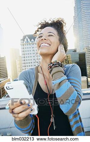 Stock Image - Mixed race woman listening to earbuds on urban rooftop. Fotosearch
