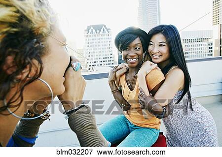 Stock Photo - Woman photographing friends on urban rooftop. Fotosearch