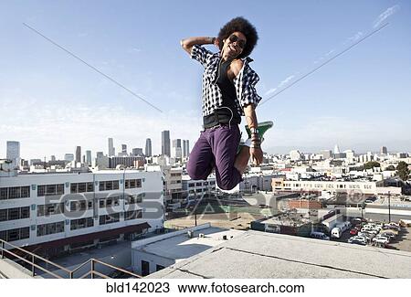 Stock Image - African American man jumping for joy on urban rooftop. Fotosearch