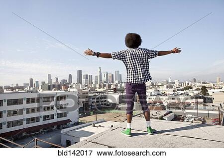 Stock Photo - African American man overlooking cityscape from urban rooftop. Fotosearch