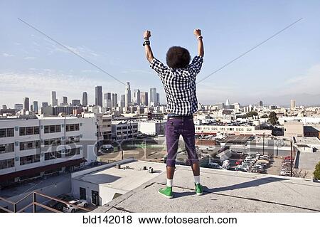 Stock Photo - African American man overlooking cityscape from urban rooftop. Fotosearch