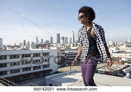 Stock Image - African American man standing on urban rooftop. Fotosearch