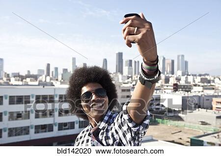 Stock Image - African American man taking cell phone picture from urban rooftop. Fotosearch