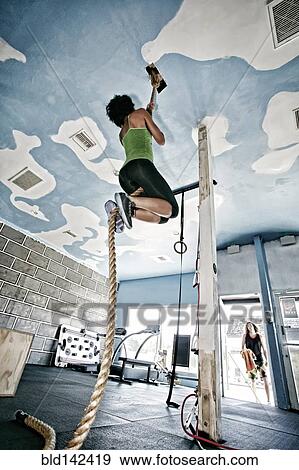 Stock Photo - African American woman climbing rope in gym. Fotosearch