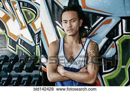 Stock Photo - Asian man standing with arms crossed in gym. Fotosearch