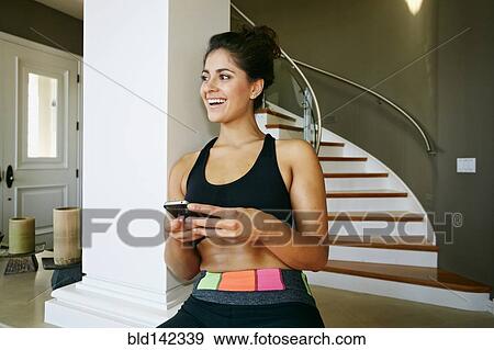 Stock Photo - Athletic mixed race woman using cell phone near pillar. Fotosearch