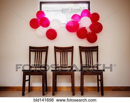 Stock Photograph - Bunches of colorful balloons over chairs near wall. Fotosearch